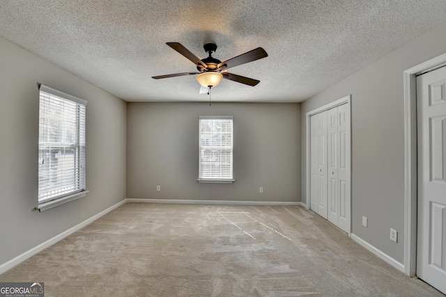 unfurnished bedroom featuring baseboards, a textured ceiling, ceiling fan, light carpet, and a closet