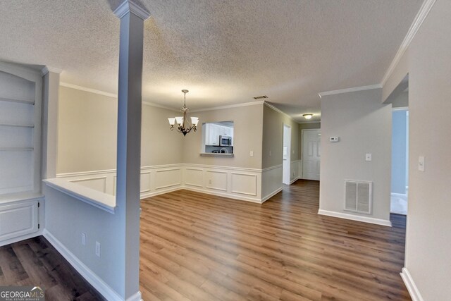 unfurnished dining area with dark wood-style flooring, a textured ceiling, visible vents, crown molding, and a notable chandelier