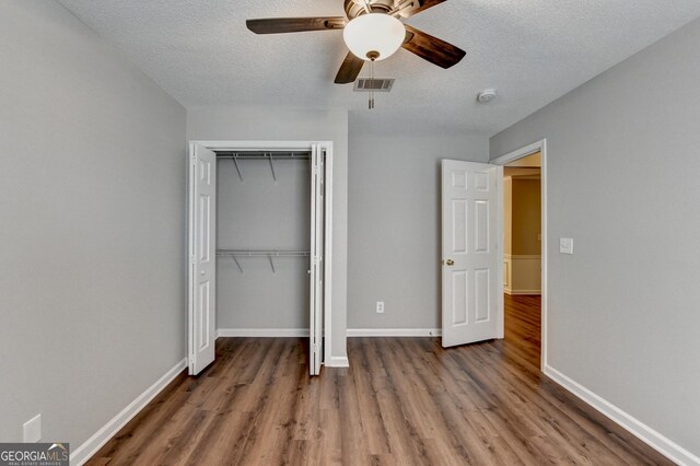 unfurnished bedroom with baseboards, a textured ceiling, visible vents, a closet, and wood finished floors