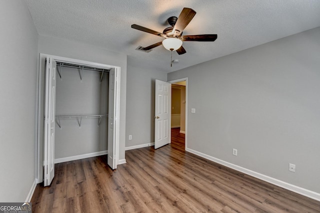 unfurnished bedroom featuring baseboards, a textured ceiling, ceiling fan, a closet, and wood finished floors