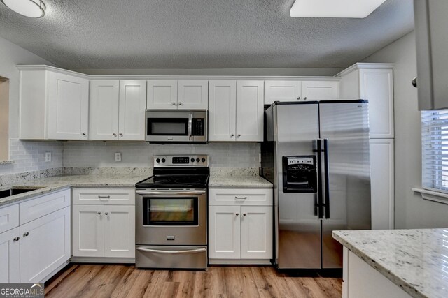 kitchen with tasteful backsplash, white cabinets, light wood-style floors, and stainless steel appliances