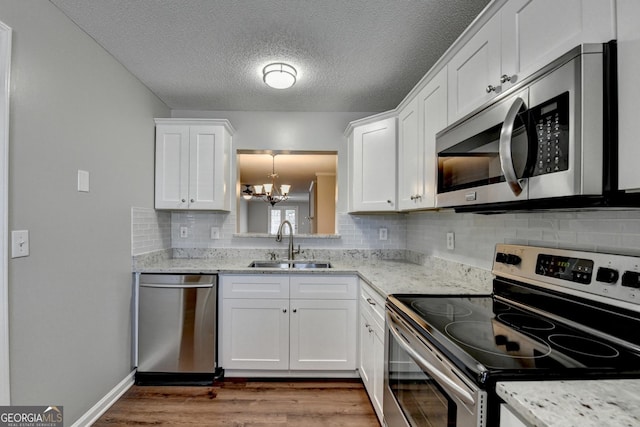 kitchen featuring an inviting chandelier, stainless steel appliances, a sink, white cabinets, and wood finished floors