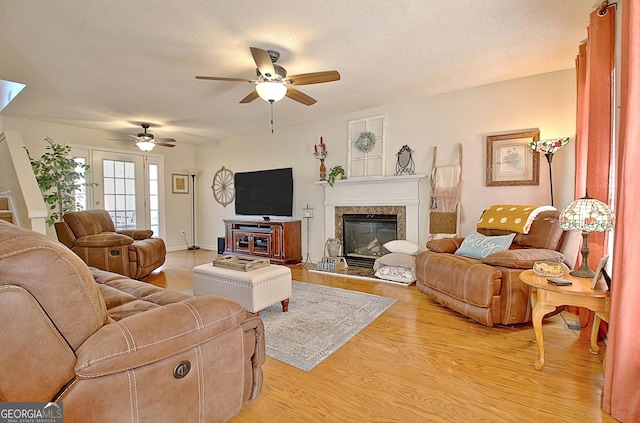 living room with a high end fireplace, a ceiling fan, light wood-style flooring, and a textured ceiling