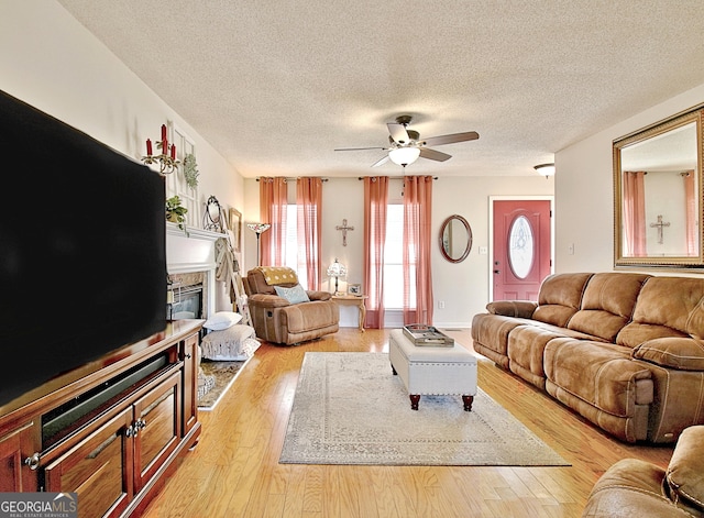 living area featuring a ceiling fan, a textured ceiling, a glass covered fireplace, and light wood finished floors