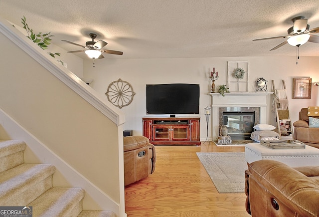 living room featuring light wood-type flooring, a ceiling fan, a textured ceiling, and stairway