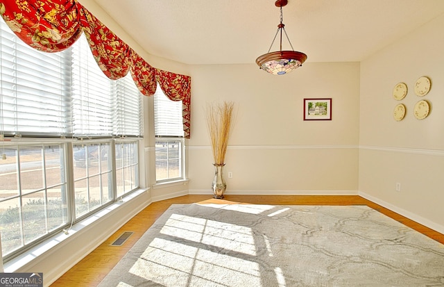 unfurnished dining area featuring visible vents, light wood-style floors, baseboards, and a healthy amount of sunlight