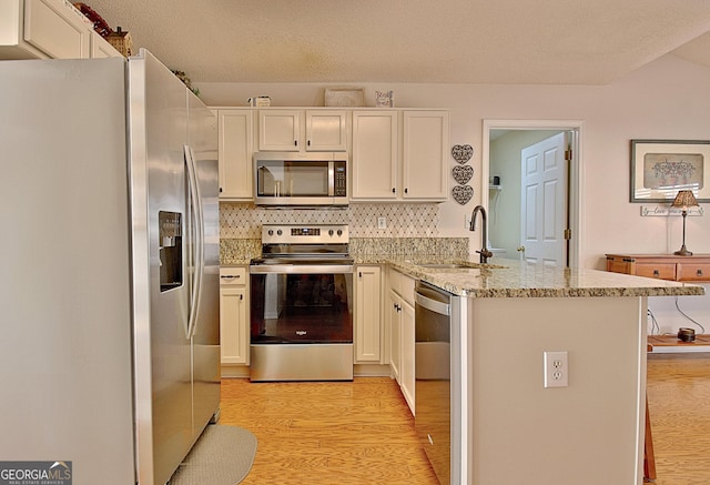kitchen with a peninsula, a sink, light wood-style flooring, appliances with stainless steel finishes, and backsplash