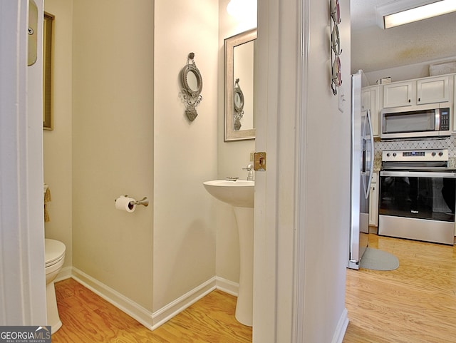 bathroom with baseboards, backsplash, wood finished floors, and toilet
