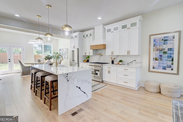 kitchen with custom exhaust hood, a kitchen bar, high end appliances, an island with sink, and light wood-style floors
