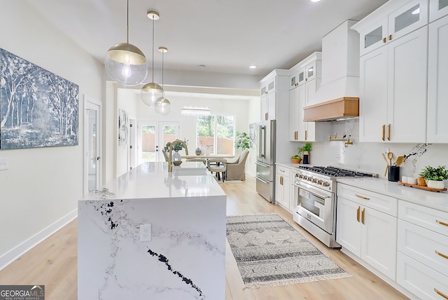 kitchen featuring white cabinetry, premium appliances, a center island with sink, light wood finished floors, and custom exhaust hood