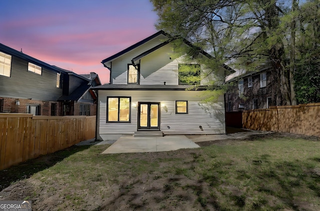 back of house at dusk with french doors, a fenced backyard, a lawn, and a patio
