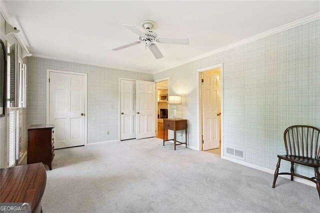 living area featuring carpet, wallpapered walls, visible vents, ceiling fan, and ornamental molding