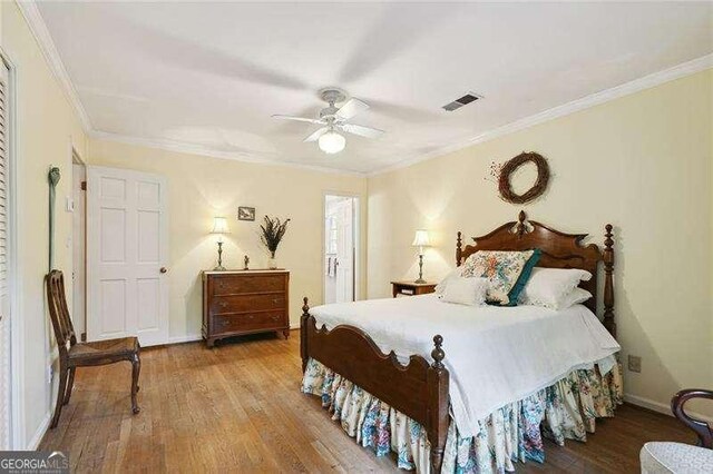 bedroom featuring baseboards, visible vents, crown molding, and wood finished floors