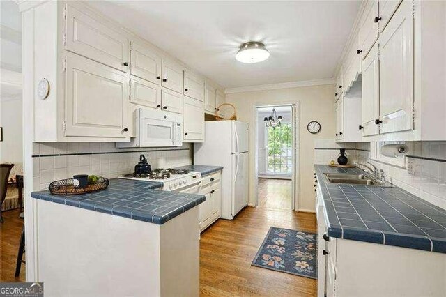 kitchen featuring white cabinets, white appliances, wood finished floors, tile countertops, and a sink