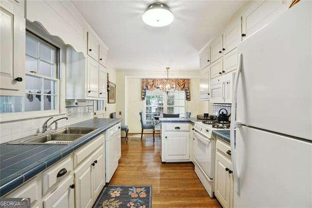 kitchen with white cabinetry, tile counters, white appliances, a sink, and a notable chandelier