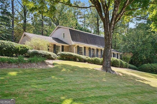 view of front facade with a gambrel roof, brick siding, and a front yard
