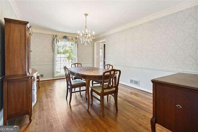 dining space featuring wallpapered walls, wainscoting, visible vents, dark wood-type flooring, and an inviting chandelier