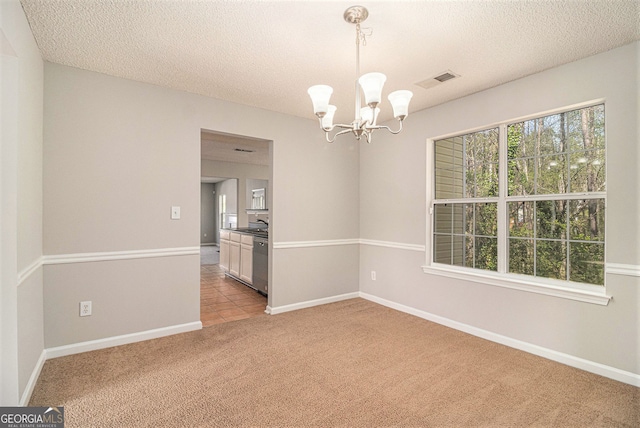 empty room with light carpet, a chandelier, a textured ceiling, and baseboards