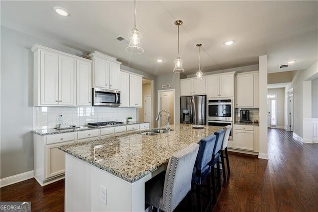 4870 Odum View Ln, Cumming, GA 30040 - kitchen featuring appliances with stainless steel finishes, an island with sink, backsplash, white cabinetry, and dark wood finished floors