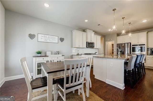 4870 Odum View Ln, Cumming, GA 30040 - kitchen with appliances with stainless steel finishes, dark wood finished floors, a center island with sink, tasteful backsplash, and light stone countertops