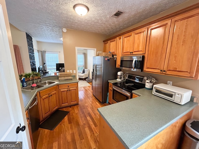 924 Morningside Dr, Griffin, GA 30224 - kitchen with stainless steel appliances, a sink, a peninsula, light wood-type flooring, and brown cabinetry