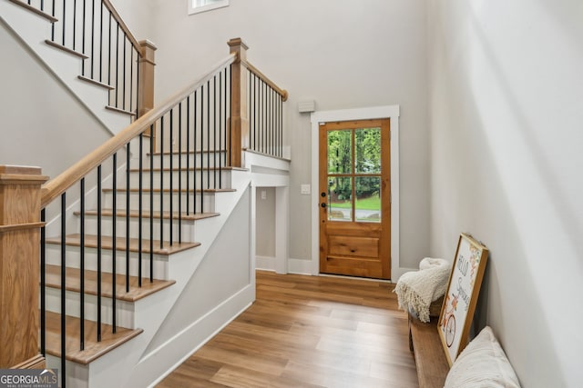 doorway with wood finished floors, a high ceiling, baseboards, and stairway