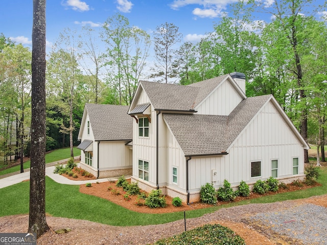 view of side of property with board and batten siding, a shingled roof, a chimney, and a yard