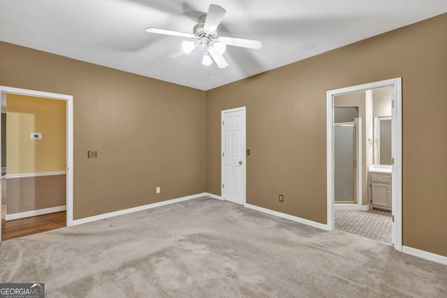 unfurnished bedroom featuring baseboards, ensuite bath, a ceiling fan, and light colored carpet