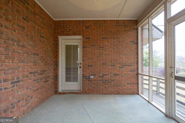 unfurnished sunroom featuring ornamental molding, carpet, and brick wall