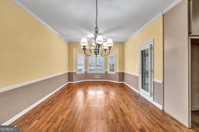 unfurnished dining area featuring crown molding, visible vents, wood finished floors, and a notable chandelier