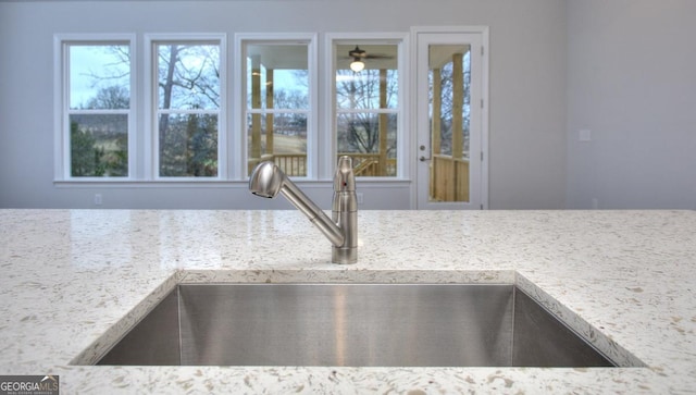interior details with ceiling fan, a sink, and light stone counters