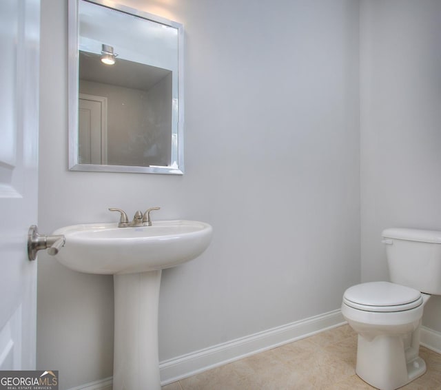 half bathroom with baseboards, toilet, a sink, and tile patterned floors