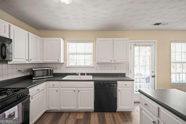 kitchen with a sink, visible vents, black appliances, and dark countertops