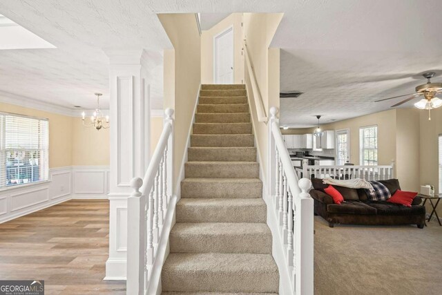 staircase featuring a decorative wall, a wainscoted wall, ceiling fan with notable chandelier, and a textured ceiling