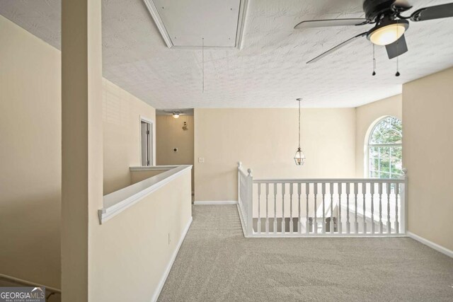 corridor with attic access, baseboards, carpet flooring, and a textured ceiling