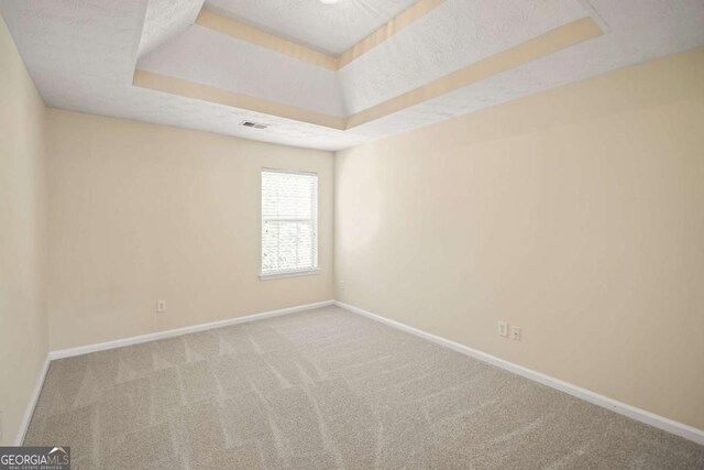 carpeted empty room featuring baseboards, a textured ceiling, visible vents, and a raised ceiling