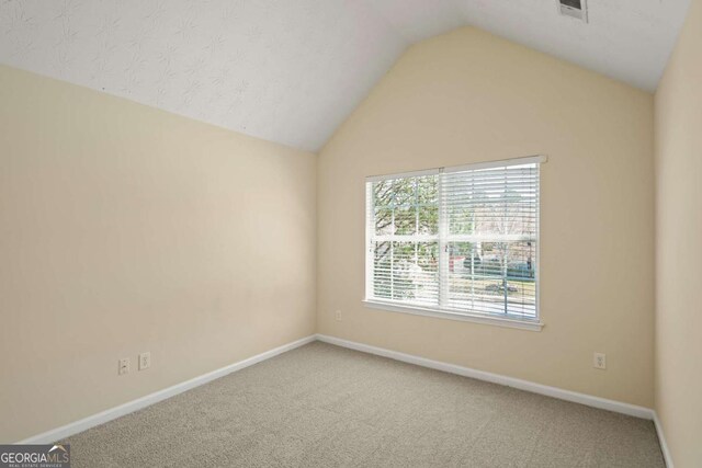 carpeted empty room featuring baseboards, visible vents, and vaulted ceiling