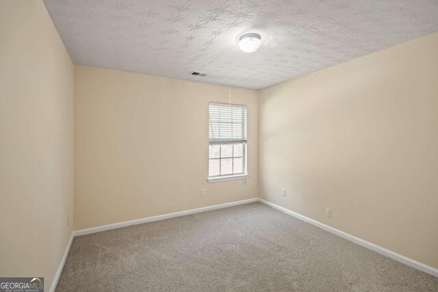carpeted spare room with a textured ceiling, baseboards, and visible vents