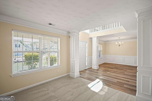 empty room featuring crown molding, decorative columns, carpet, a chandelier, and visible vents