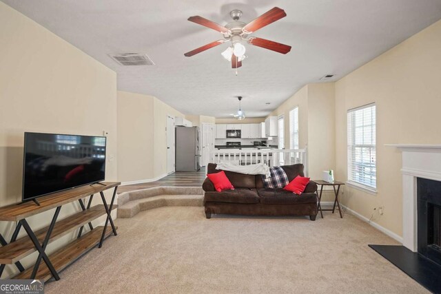 living room with a fireplace with flush hearth, baseboards, light colored carpet, visible vents, and ceiling fan