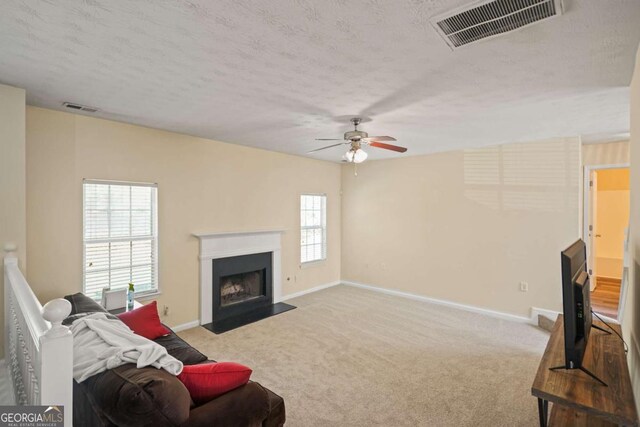 living room with a ceiling fan, carpet, a textured ceiling, and visible vents