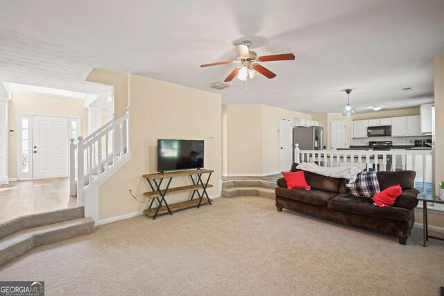 living room featuring baseboards, stairway, light colored carpet, and ceiling fan