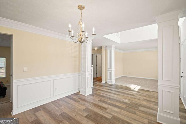 unfurnished dining area with decorative columns, a chandelier, wood finished floors, a skylight, and ornamental molding