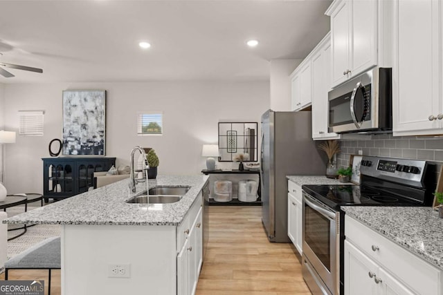 kitchen featuring white cabinetry, a center island with sink, a sink, a ceiling fan, and appliances with stainless steel finishes