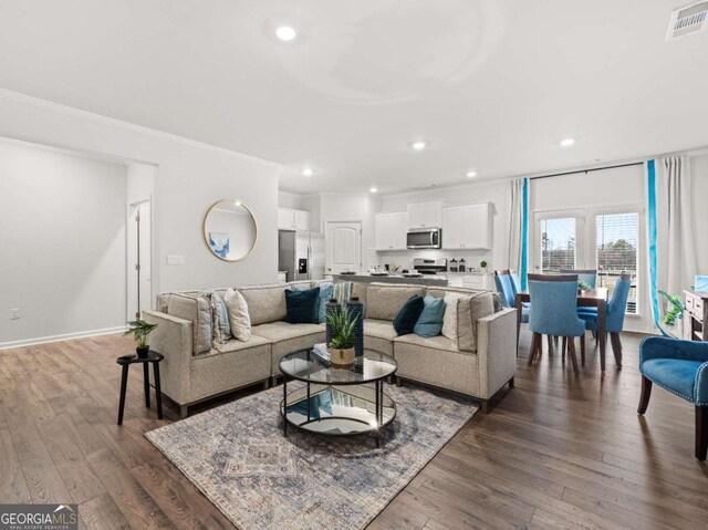 living area with dark wood-style flooring, visible vents, baseboards, ornamental molding, and recessed lighting