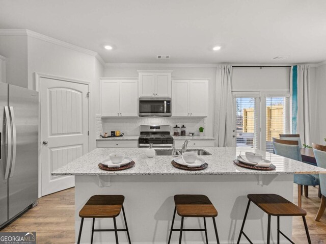 kitchen featuring a kitchen bar, tasteful backsplash, appliances with stainless steel finishes, white cabinetry, and a sink