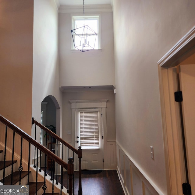 foyer entrance featuring a decorative wall, stairs, wainscoting, a towering ceiling, and dark wood finished floors