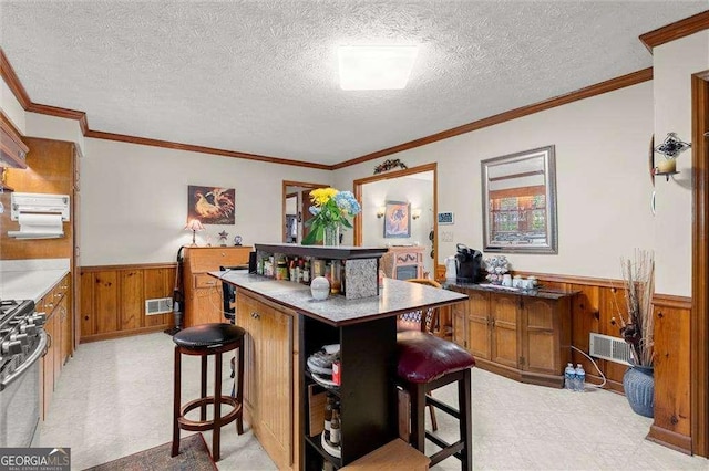 bar featuring visible vents, wood walls, stainless steel gas stove, light floors, and a wainscoted wall