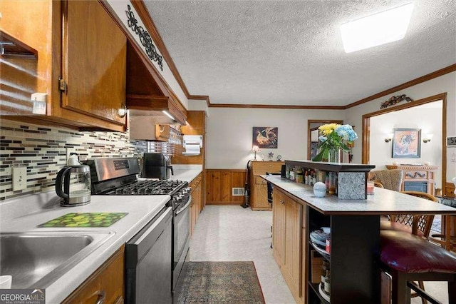 kitchen featuring gas stove, wainscoting, dishwasher, and brown cabinets