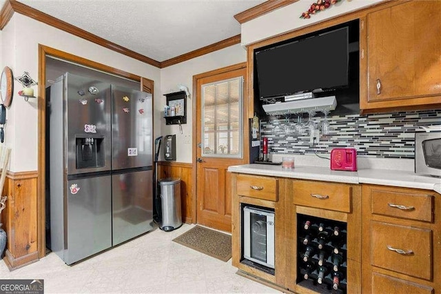 kitchen featuring stainless steel fridge with ice dispenser, light countertops, brown cabinetry, a wainscoted wall, and ornamental molding